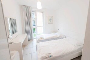A hotel room with two beds, a desk, a mirror, and a window with curtains.