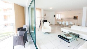 Ein modernes Wohnzimmer mit einem Glastisch, einem weißen Sofa und einem Essbereich mit weißen Stühlen.