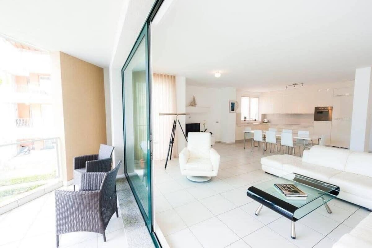 Un salon moderne avec une table basse en verre, un canapé blanc et un coin repas avec des chaises blanches.