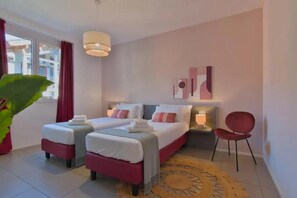 Habitación de hotel con dos camas, una silla roja, una planta grande en maceta y vistas al exterior.