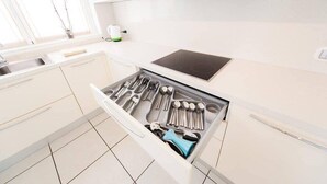Eine Küche mit weißen Schränken, einem eingebauten Herd und einem Schubladenorganisator mit Besteck.