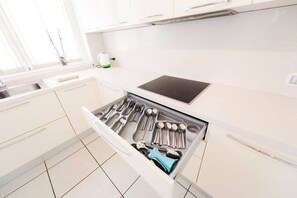 Une cuisine avec des meubles blancs, une cuisinière encastrée et un organiseur de tiroir contenant des ustensiles.