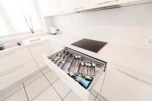 Eine moderne Küche mit weißen Schränken, einem eingebauten Kochfeld und einem Schubladeneinsatz für Kochutensilien.