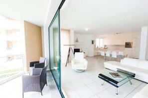 A modern living room with a glass coffee table, a white sofa, and a dining area with chairs. - Maccagno Apartments (Maccagno con Pino e Veddasca)