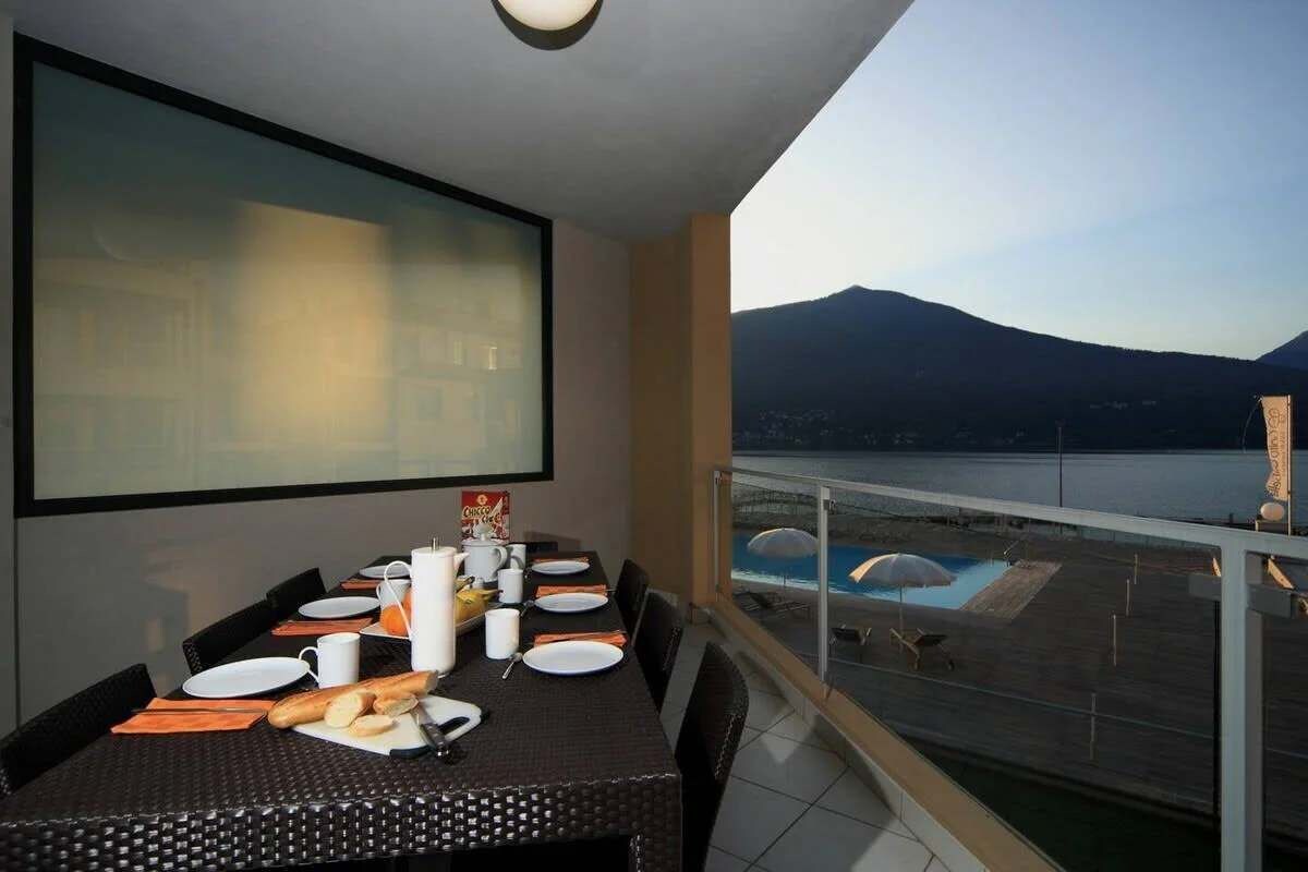 Un coin repas avec une table dressée pour quatre personnes, donnant sur une piscine et des montagnes.