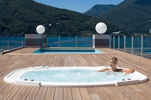 A hot tub on a wooden deck with a view of a lake and mountains. - Maccagno Apartments (Maccagno con Pino e Veddasca)
