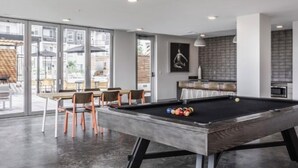 A modern indoor pool table with a billiards cue and balls, surrounded by wooden chairs. - The 513 Flat! Pool & River View! Free Gated Parking! Walk to Banks & Stadiums! (Cincinnati)