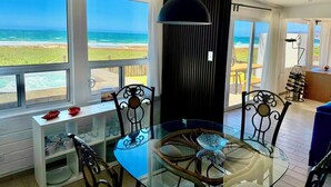 A dining area with a glass table, chairs, and a view of the ocean. - Casa Azul - beachfront jacuzzi & sunsets (Ensenada)