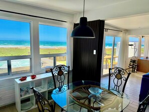 A dining area with a glass table, chairs, and a view of the ocean.