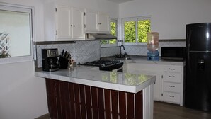 Une cuisine moderne avec des meubles blancs, un réfrigérateur noir, un distributeur d’eau et un four à micro-ondes.