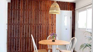 Un espace repas avec une table ronde en bois, des chaises blanches et un luminaire suspendu.