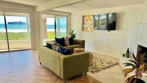 A spacious living room with a herringbone wooden floor, a sofa with cushions, a flat-screen TV, and a fireplace. - Casa Peninsula- Beach House (Ensenada)