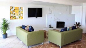 A living room with two green sofas, a flat-screen TV, a fireplace, and a floral artwork on the wall. - Casa Peninsula- Beach House (Ensenada)