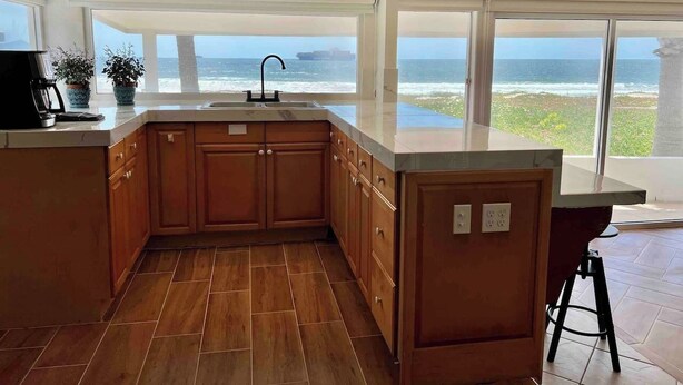 A kitchen with wooden cabinets, a sink, and a view of the ocean. - Casa Peninsula- Beach House (Ensenada)