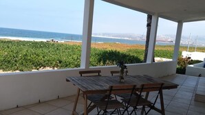 A covered patio with a wooden table and chairs, overlooking a coastal landscape with greenery and the sea. - Casa Peninsula- Beach House (Ensenada)