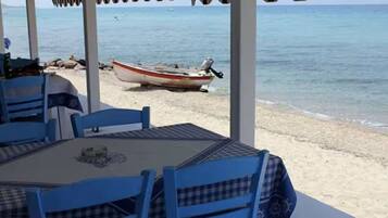 En restaurant ved stranden med blå stole og et bord, med udsigt over havet og en båd på kysten.
