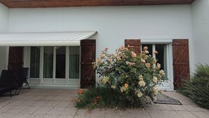 Una casa moderna con un porche cubierto, un jardín con plantas en flor y una puerta de madera.
