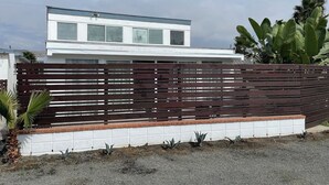 Une maison moderne à deux étages, avec une façade blanche et une clôture marron.