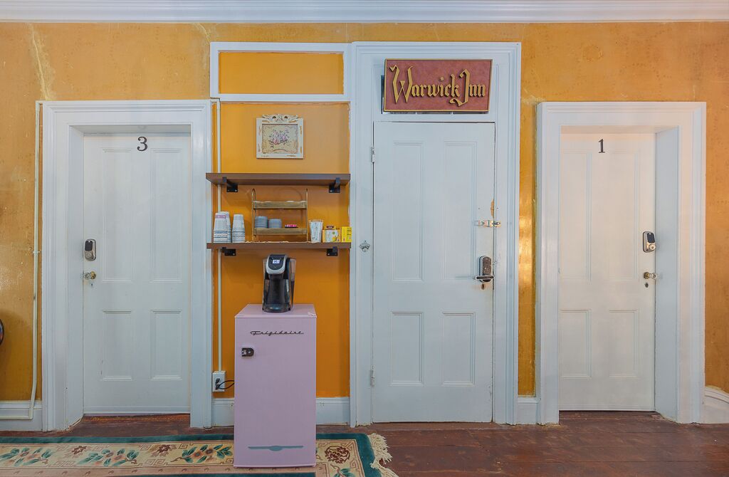 Un hall d’hôtel avec trois portes, un distributeur de café et une étagère contenant des articles de toilette.
