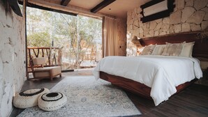 A bedroom with a large bed, a wooden chair, a small table, and a view of the outdoors through a glass door. - Tulum Jungle Villa Aire (Tulum)