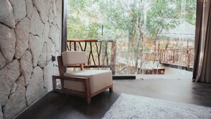 A room with a stone wall, a wooden chair, and a view of a thatched-roof structure through a glass door. - Tulum Jungle Villa Aire (Tulum)