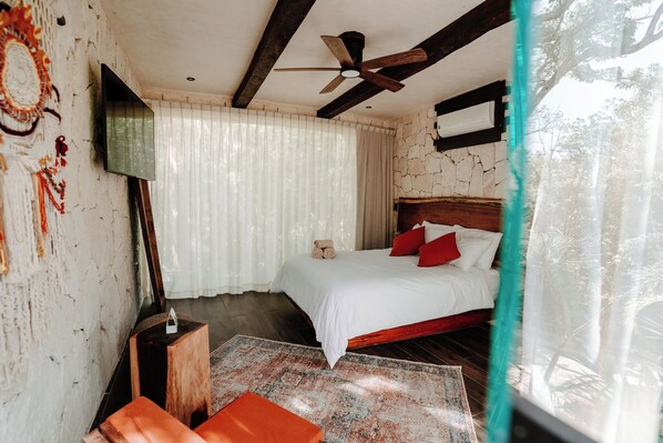 A bedroom with a bed, a ceiling fan, a TV, and a window with curtains. - Tulum Jungle Villa Fuego (Tulum)