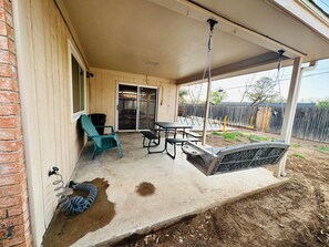 A covered patio with a table and chairs, a swing, and a sliding glass door leading to an outdoor area. - #3 Charming 4BR 2BA Home in Midland – Comfort, Convenience & Great Location! (Midland)