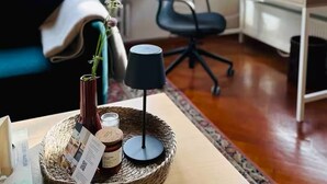 Un salon moderne avec un canapé bleu, un bureau et un ordinateur. De grandes fenêtres offrent une vue sur la verdure environnante.