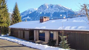 A building with a snow-covered roof, a small tower-like structure on the roof, and a mountainous backdrop. - Alpenjuwel Oberstdorf – Mountain Views, Balcony & Sauna, Lift Pass, Dog Friendly (Oberstdorf)