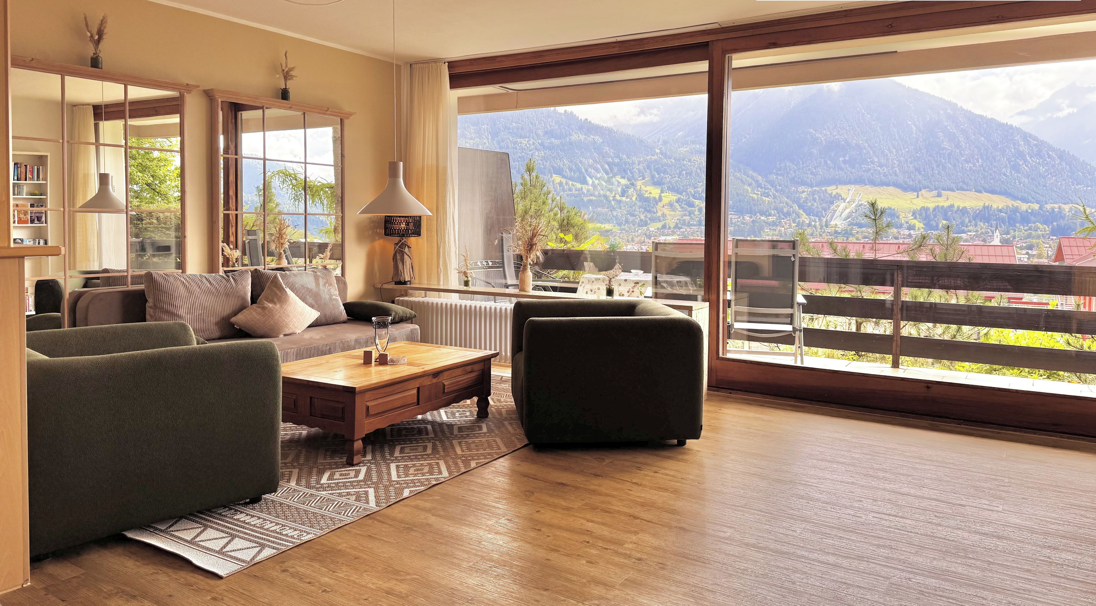 Sala de estar moderna com uma grande janela que oferece vista para a montanha, um sofá, uma mesa de centro e um abajur.