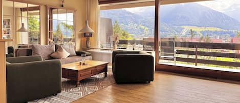 Sala de estar moderna com uma grande janela que oferece vista para a montanha, um sofá, uma mesa de centro e um abajur.