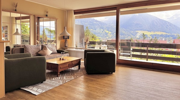 A modern living room with a large window offering a mountain view, a sofa, a coffee table, and a lamp.