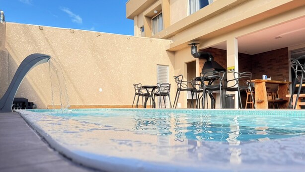 Une piscine agrémentée d’un élément décoratif aquatique, un espace extérieur aménagé pour se détendre et un coin barbecue.
