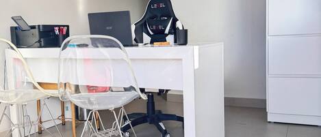Un espacio de oficina moderno con un escritorio blanco, una silla gamer negra y dos sillas traslúcidas.