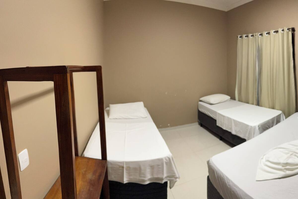 A hotel room with two single beds, a wooden chair, a mirror, and a window with curtains.