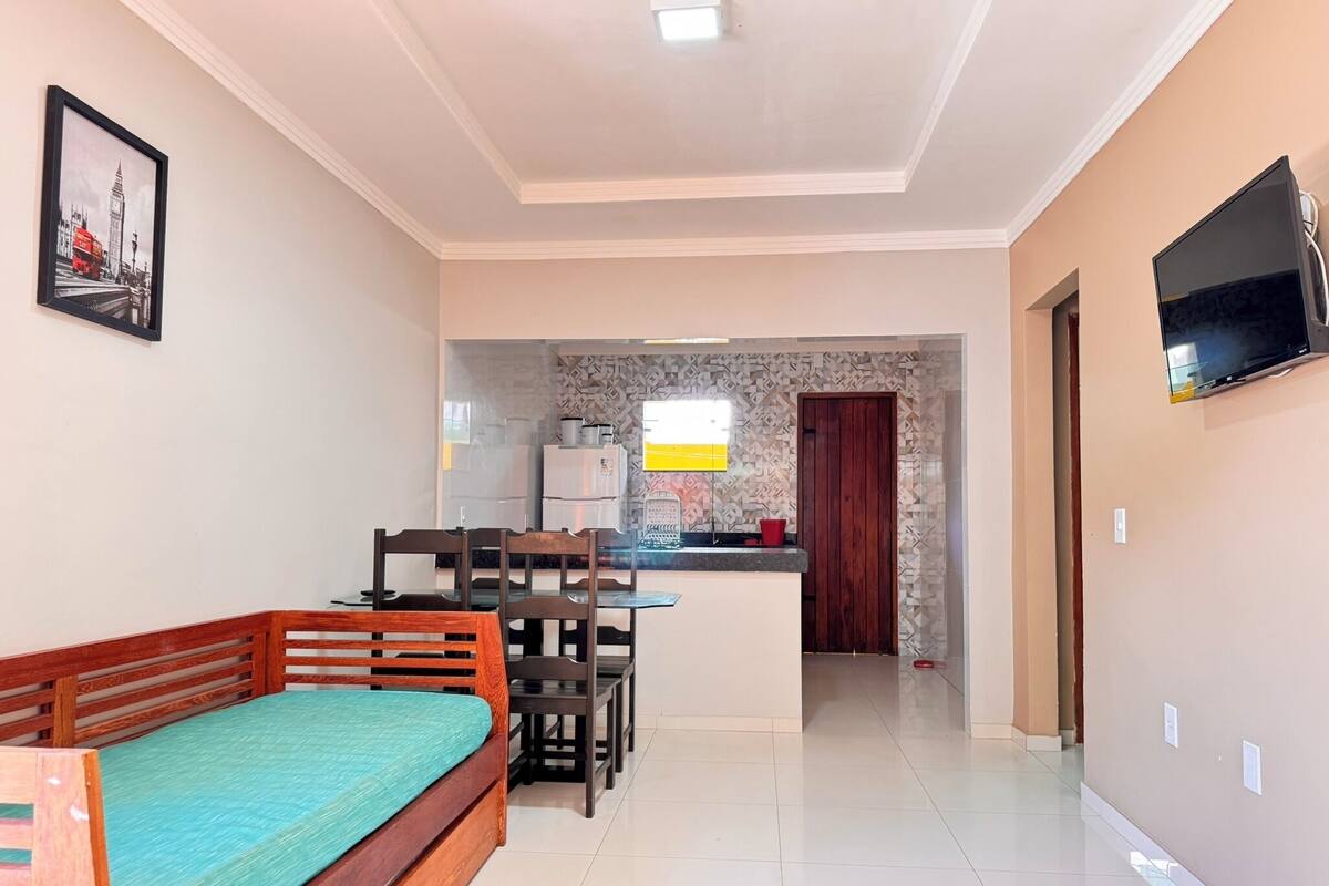 A compact living space with a bed, a dining area, a kitchen, and a TV mounted on the wall.