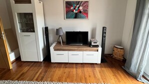 A living room with a wooden floor, white entertainment unit, a flat-screen TV, a lamp, a globe, a painting, and a speaker. - Cozy vacation apartment in Winkel in the heart of the Rheingau. (Oestrich-Winkel)