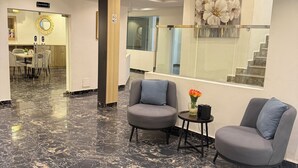 A modern lobby with a marble floor, two grey armchairs, a small table with a vase, a staircase, and a restaurant sign. - SAAFI Boutique Hotel (Abuja)