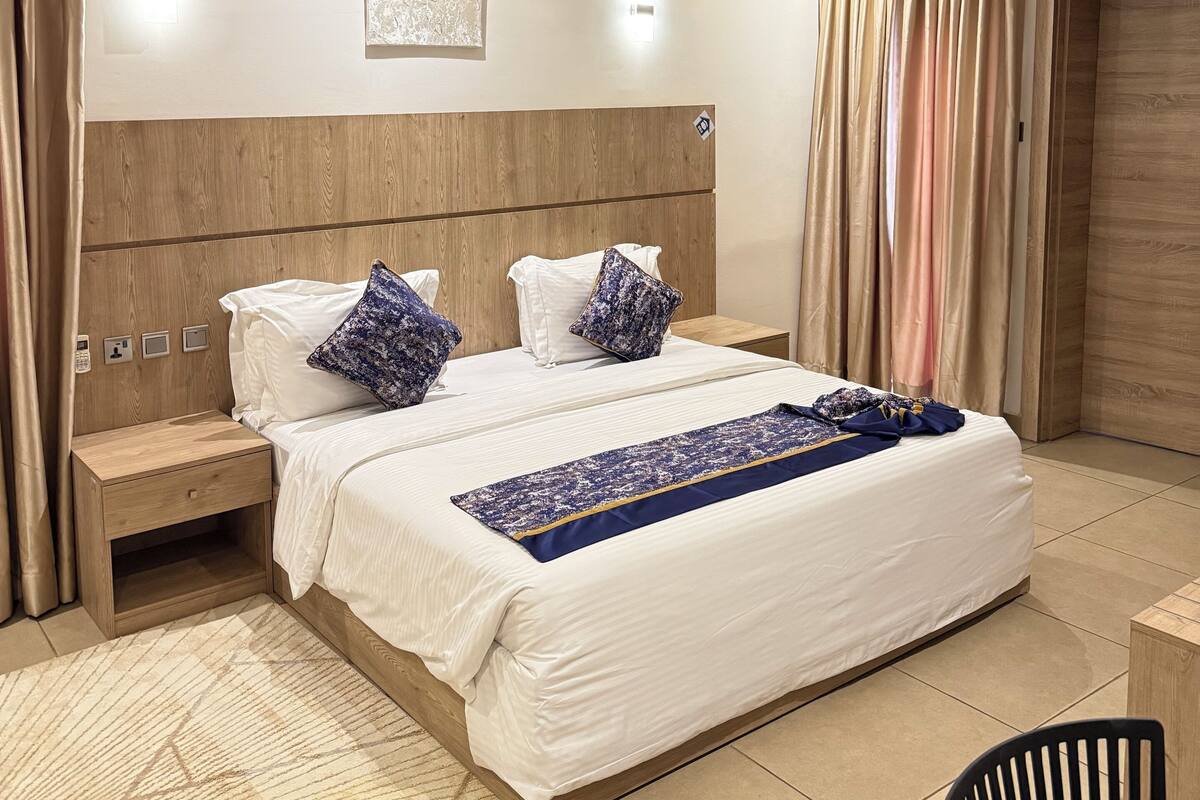 Een hotelkamer met een groot bed, houten hoofdbord, nachtkastjes en een nachtkast.