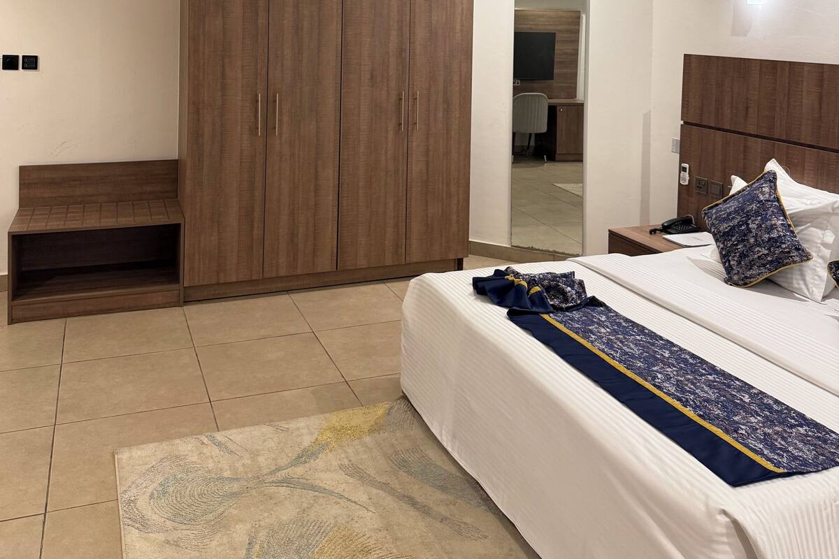 Een slaapkamer met een grote garderobe, een bed met een geborduurd beddegoed en een klein zithoekje.