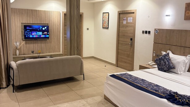 A modern hotel room with a large bed, a sofa, a TV mounted on the wall, and a wooden accent wall. - SAAFI Boutique Hotel (Abuja)