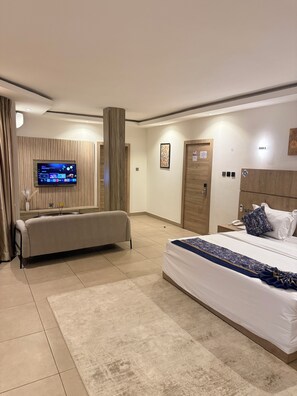 Una habitación de hotel moderna con una cama grande, un sofá, un televisor montado en la pared y una pared decorativa de madera.