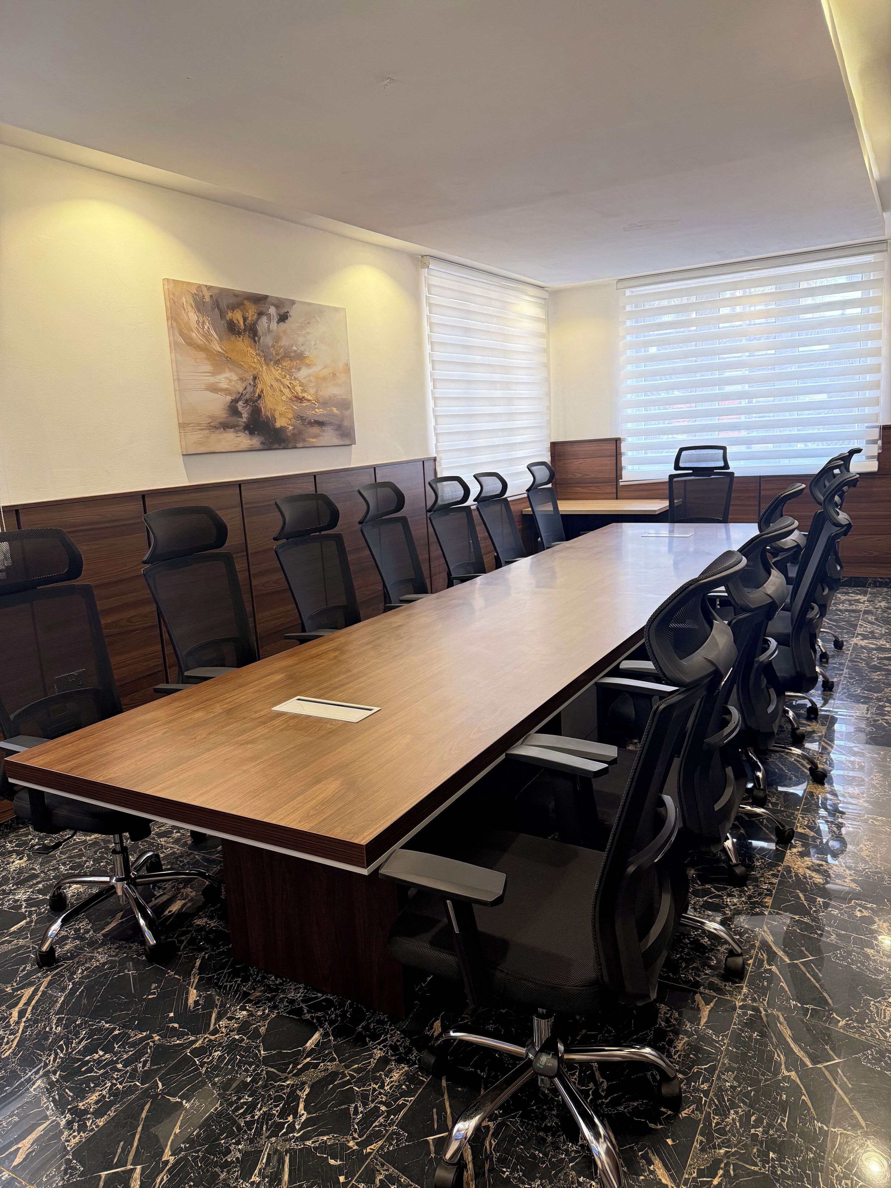 Un salón de conferencias con una larga mesa de madera, sillas de oficina negras y piso de mármol.