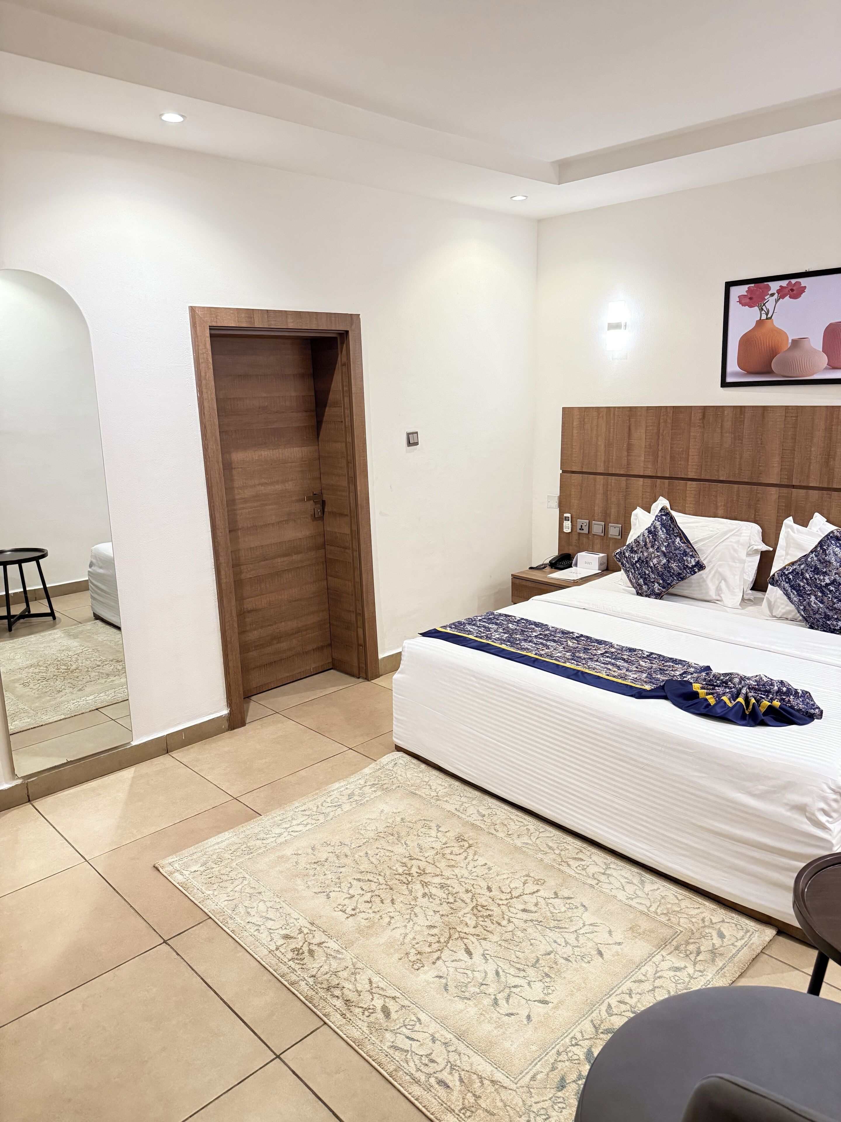 A modern bedroom with a large bed, a wooden wardrobe, a bedside table, and a nightstand.