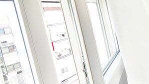 Blick durch ein Fenster mit Jalousien, der einen mehrstöckigen Gebäudebau mit rotem Dach zeigt.