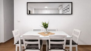 Ein Essbereich mit einem weißen Tisch, vier weißen Stühlen, einer Vase mit Grünpflanzen und einem gerahmten Spiegel an der Wand.