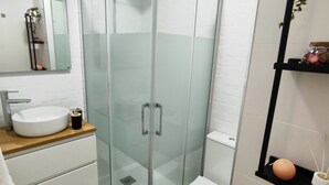Ein modernes Badezimmer mit einer Duschkabine, einem weißen Waschbecken und einer Toilette.