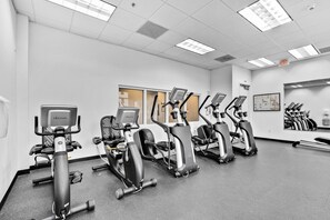 A gym with multiple treadmills and stationary bikes, a wall-mounted mirror, and a framed poster on the wall.