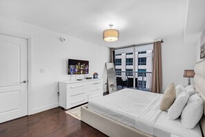 Habitación de hotel con cama, cómoda, televisor y vista del paisaje urbano a través del ventanal.