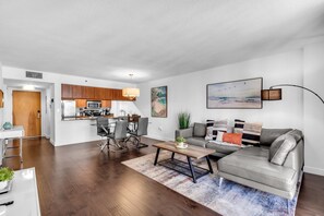 A modern living room with a grey sofa, a coffee table, and a dining area with a glass table and chairs. - Relaxing 1-Bed Condo W/ City Views in Brickell Key (Miami)